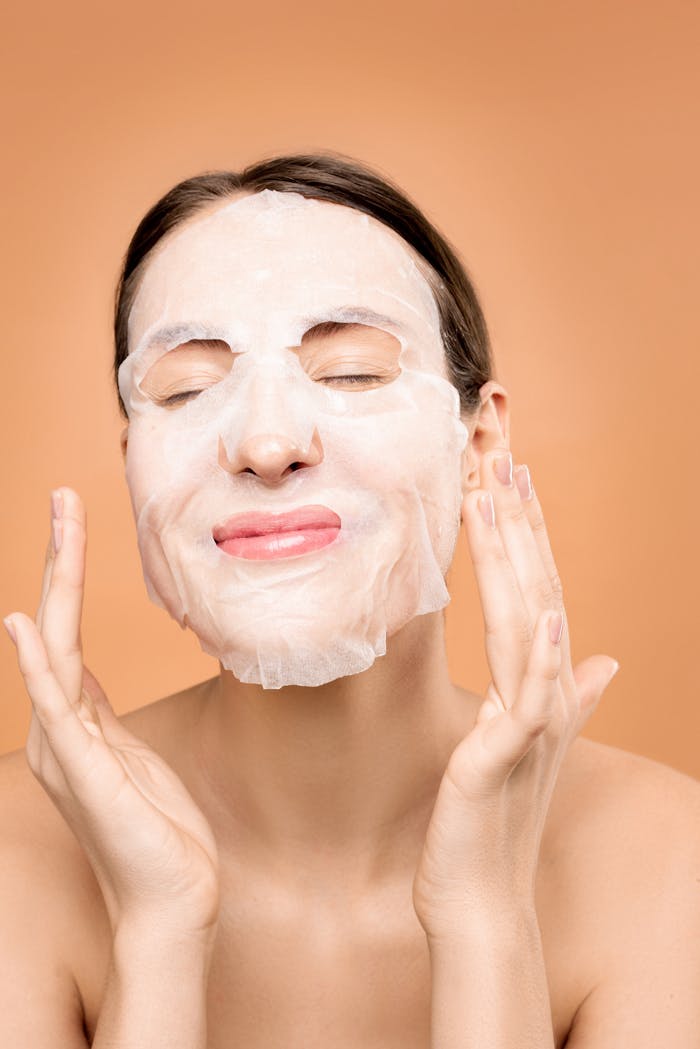 Woman smiling with a sheet face mask, embracing a skincare self-care moment.